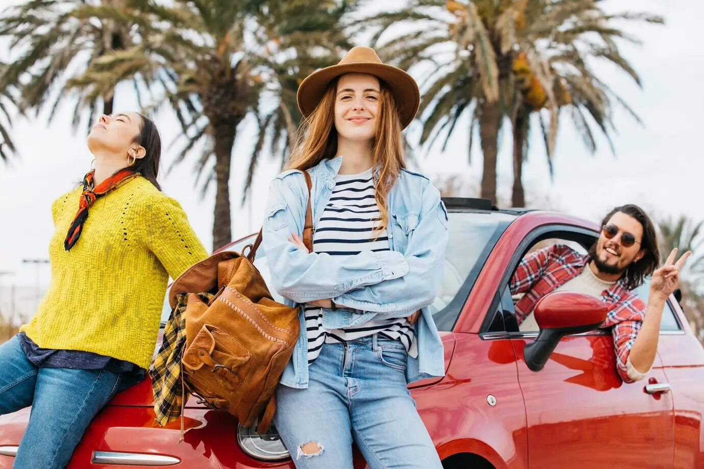 Женщины рядом с мужчиной, который высовывается из машины и показывает жест мира.